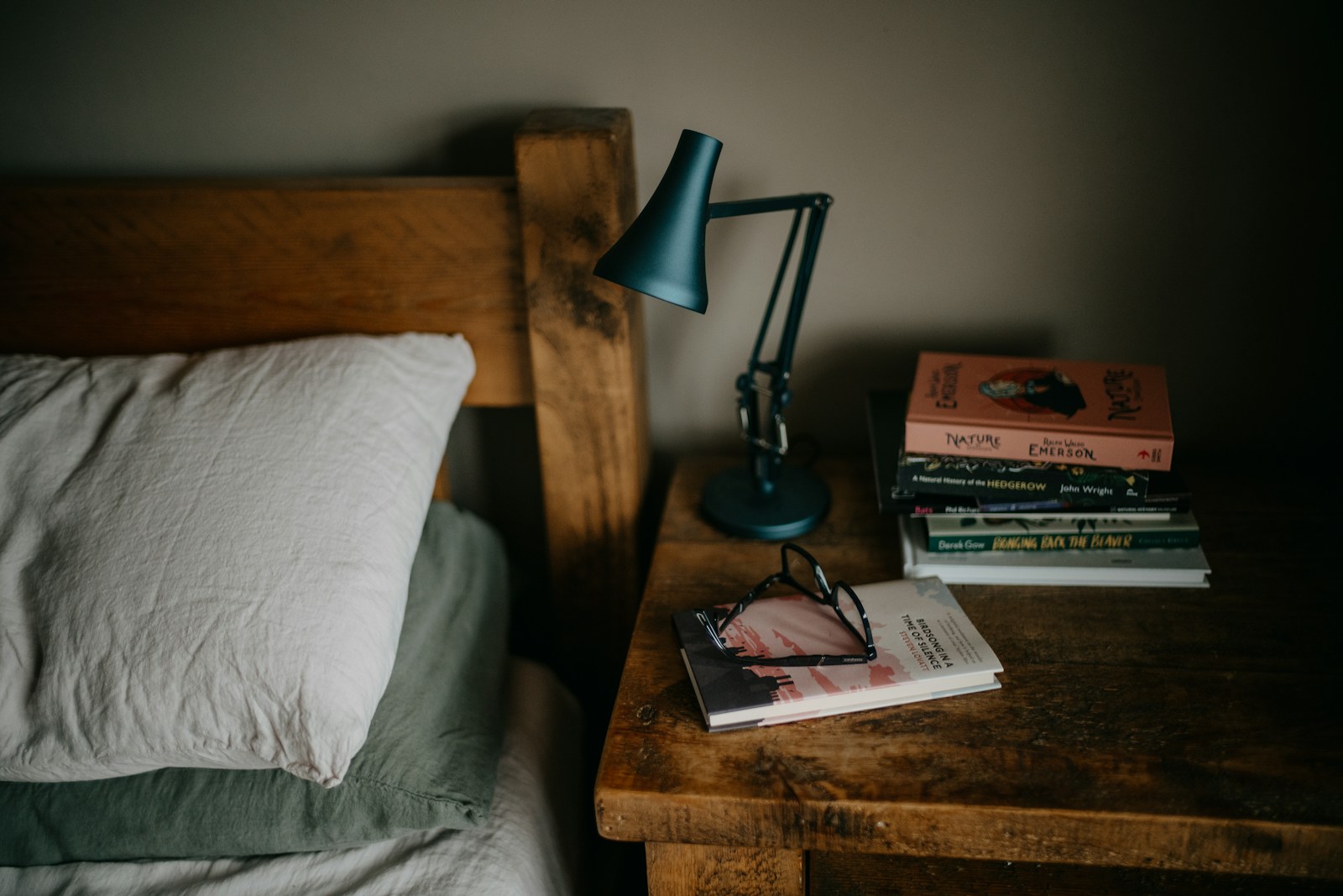 Books, reading glasses and a lamp beside a linen-covered bed