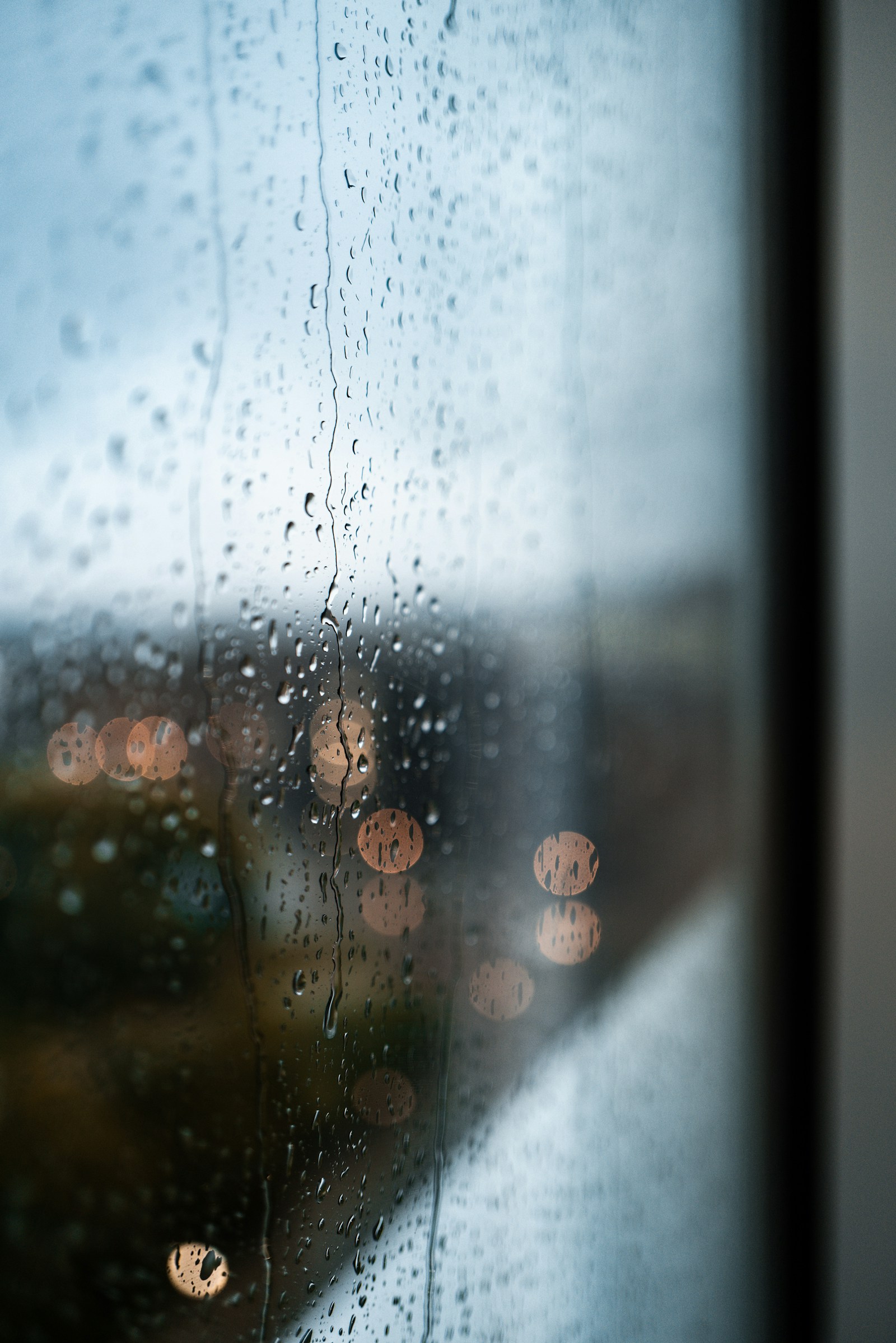 Rain on a window with soft blue and amber lights beyond