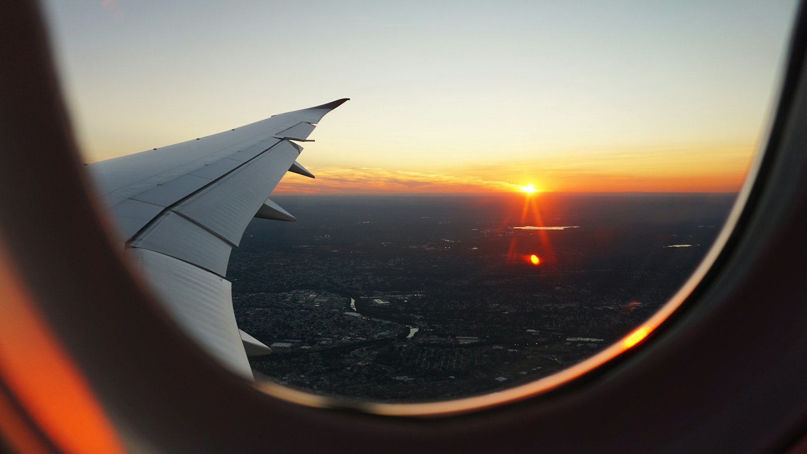 An airplane wing and sunset seen through a cabin window